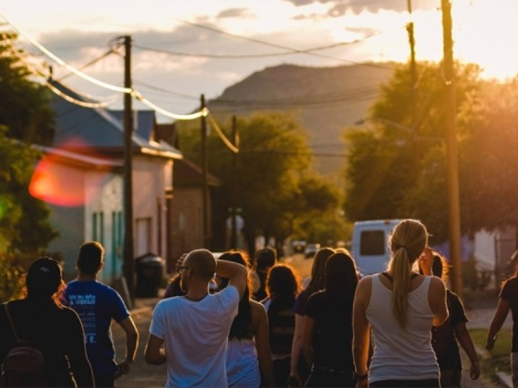 a group of people walking down the street toward a setting sun