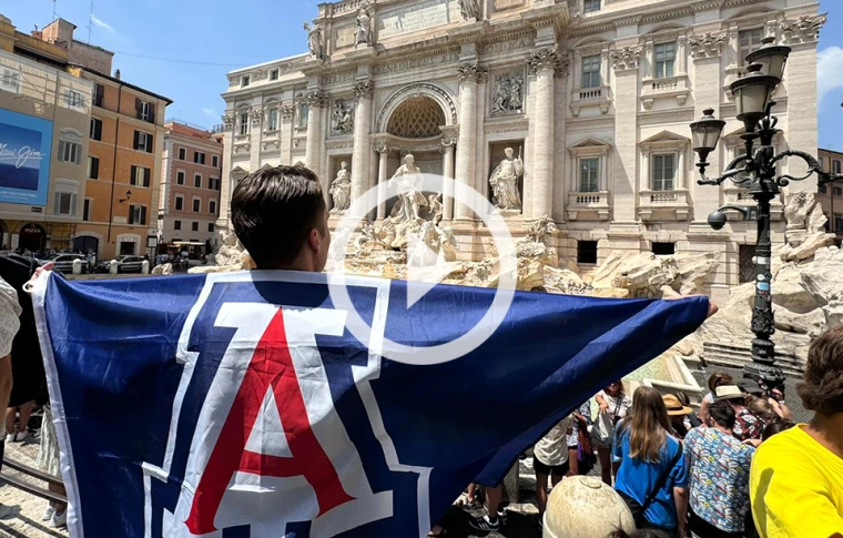 Student standing outside with a U of A block A flag over their back and shoulders